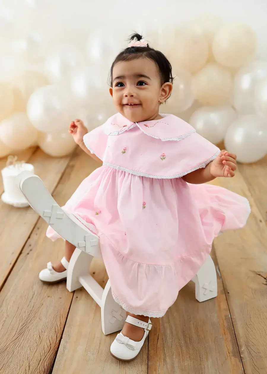 Isabela sorrindo, de vestido rosa bordado com florzinhas